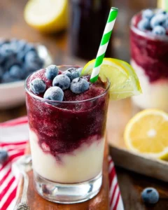 Boozy blueberry limeade slushie in a glass with lime slices and blueberries